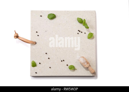 Concrete stone server/board/tray with space for text on white background. Arranged basil leaves, wooden scoop, peppercorns and salt crystals. Top view Stock Photo