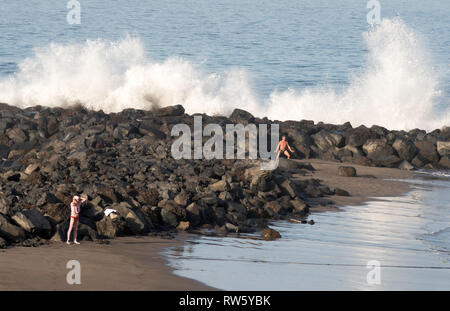 People exercising on the beach while waves crash into rocks behind, Costa Adeje, Tenerife, Canary Islands. Stock Photo