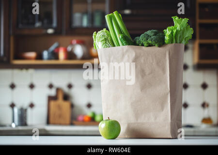 Fresh green vegetables and fruits in a paper bag on the kitchen table. Selective focus. Stock Photo
