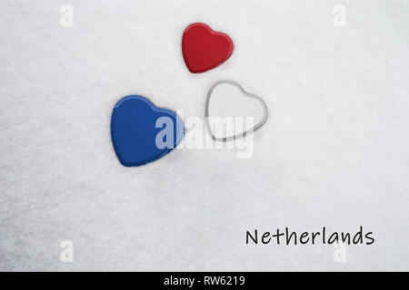 Colors of the dutch flag (Upsdell Red, White, Dark Cornflower Blue) painted on three hearts. Snow background with the country, Netherlands, written Stock Photo
