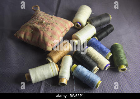 A group of sewing threads of different colors next to a pincushion or pincushion to nail the needles while they are not used, all on a dark blue cloth Stock Photo