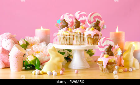 Easter theme candy land drip cupcakes decorated with chocolate bunnies in party table setting. Stock Photo