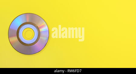 Top down view, small CD shiny / rainbow side, on yellow board, space for text on right side. Stock Photo