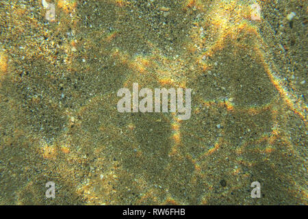 Underwater photo sea bottom seen from the top, light refraction creates small rainbows on the sandy floor. Abstract marine background. Stock Photo