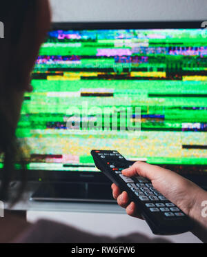 Vertical image of woman wearing holding remote control looking at the bad signal static noise coming from her digital DTV televisions flat screen Stock Photo