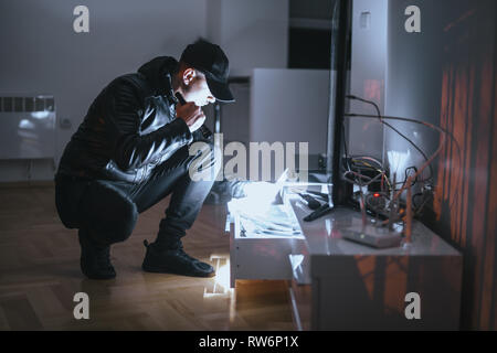 Burglar wearing black clothes and breaking into a house at night Stock Photo