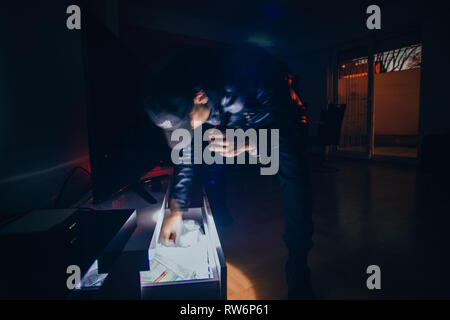 Burglar wearing black clothes and breaking into a house at night Stock Photo