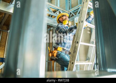 Skeleton Steel Building Construction Worker Wearing Safety Hard Hat and Noise Reduction Headphones. Going Up Using Ladder. Stock Photo