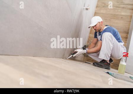 Caucasian Worker in His 30s Sealing Wall Corners of Ceramic Tiles Inside Newly Remodeled Bathroom. Using Silicone Sealant. Stock Photo