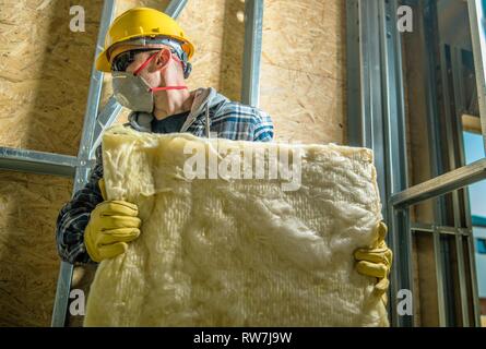 Caucasian Construction Worker Wearing Safety Mask Moving Pieces of Mineral Wool Insulation. Stock Photo