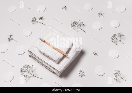 White towels, wooden toothbrush, cotton pads, swabs, and baby's breath flowers on white background. Beauty and body care. Stock Photo