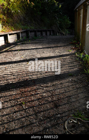 Shadowed path with creative patterns made by the sun shining through the fence. Stock Photo