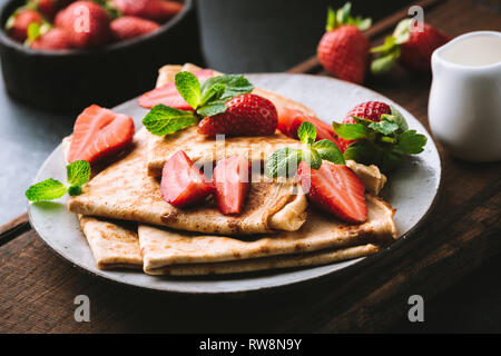 Crepes or blini with strawberries on plate. Dark moody food photo. Tasty breakfast or dessert Stock Photo