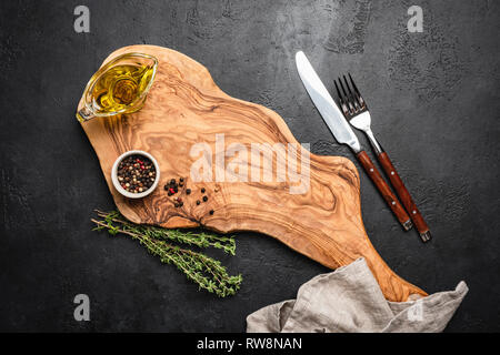 Table setting, eating utensils. Wooden board, cutlery, spices on black concrete background. Top view. Food background, menu concept Stock Photo