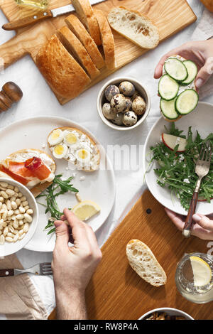 Couple eating delicious and healthy breakfast or lunch top view. Various snacks, appetizers, arugula salad, sandwiches with prosciutto and vegetables Stock Photo
