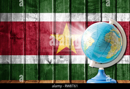 Globe with a world map on a wooden background with the image of the flag of Suriname. The concept of travel and leisure abroad. Stock Photo