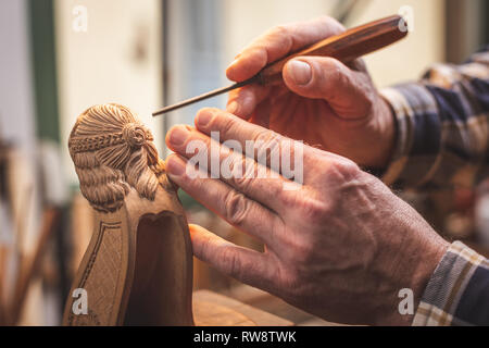 Hands of a wood sculptor with a tool working on a small wooden figure Stock Photo