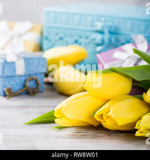 Yellow tulips in a blue metal box and gift boxes on the light gray background. Greeting card for mother's day. Copy space. Stock Photo