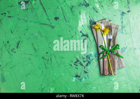 Cutlery with daffodils on a napkin. Top view, green concrete surface background, copy space for you text Stock Photo
