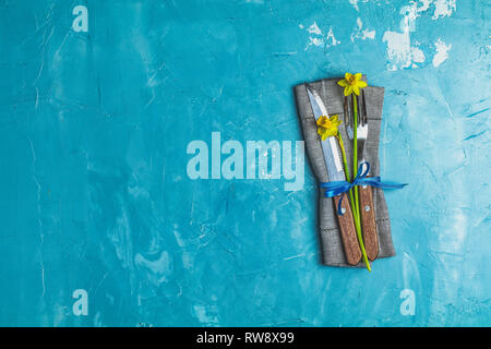 Cutlery with daffodils on a napkin. Top view, blue concrete surface background, copy space for you text Stock Photo