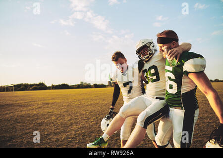 American football players carrying an injured teammate off the field during a practice session in the late afternoon Stock Photo