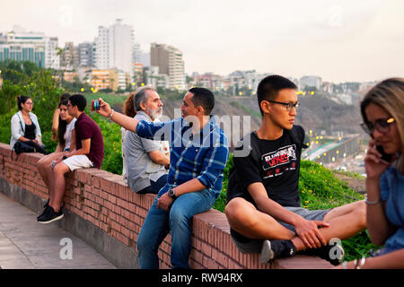 Lima, Peru - February 22 2019: Peruvian people and tourists watching the sunset and taking selfies at Malecón de la Costa Verde Stock Photo