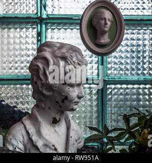 Chipped white head sculpture against glass block wall with antique plaster head molding. Vintage concept. Stock Photo