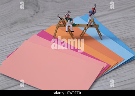 Colour paint swatch cards with miniature scale model painters and decorators on a grey wood background with pinks oranges and blues Stock Photo