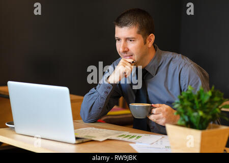 Smiling businessman holding cup of coffee while working on laptop at modern cafe Stock Photo