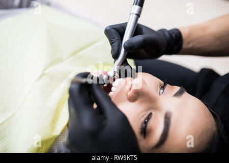 Young man dentist working in the dentist office, doing teeth repair, putting teeth implants on a young woman with open mouth. Dental implants and toot Stock Photo