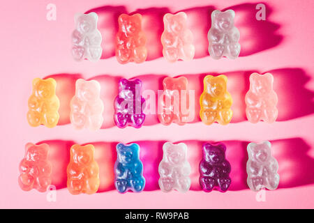 A close-up of three rows of brightly-colored gummy bears, photographed on a pink background with poppy studio light. Stock Photo