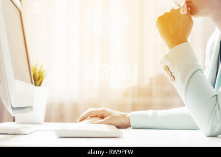 A woman works in an office. Looks at the computer screen. Sunlight in the window. Closeup Stock Photo