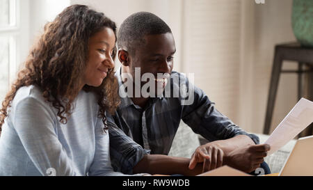 Happy mixed race couple check paper bills paying online Stock Photo