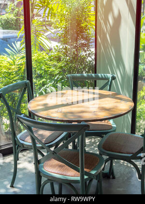 Vintage wooden table and four green chairs in the corner of restaurant with window glass near the garden in vertical style. Stock Photo