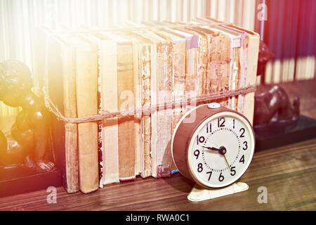 Old books tied up with rope on shelf and alarm clock Stock Photo