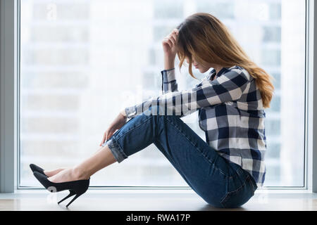 Depressed vulnerable young woman in trouble sitting on floor alone Stock Photo