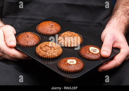 Homemade chocolate,  banana and caramel muffins in a baking dish in the hands of the confectioner. Dessert for gourmet. Selective focus Stock Photo
