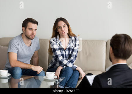 Unhappy millennial couple talking to psychologist sitting on couch Stock Photo