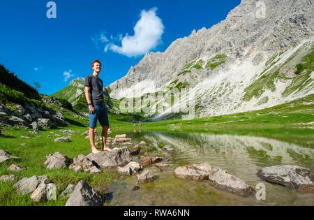Young man stands on stone, mountain lake at Prinz-Luitpold-Haus, Allgäu Alps, Bad Hindelang, Allgäu, Bavaria, Germany Stock Photo