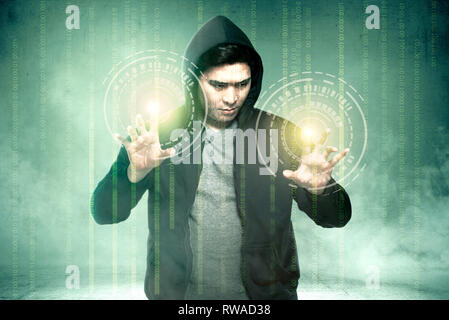 Young asian hacker in black hoodie touching virtual screen with binary code over green background Stock Photo