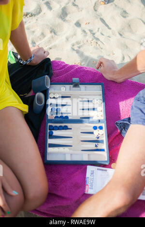 Two people playing board game on pink towel on sand at Barceloneta beach, Barcelona, Spain Stock Photo