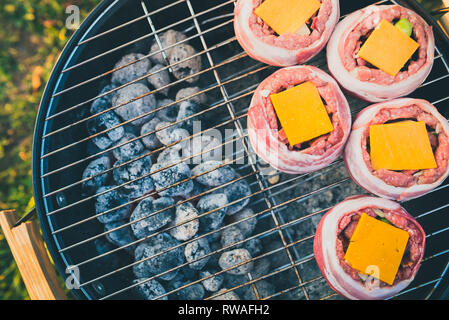 Making home made Beer Can Bacon Burgers on barbecue grill. Preparing stuffed patties, wrapped  in bacon and grilling on indirect heat in nature at bac Stock Photo