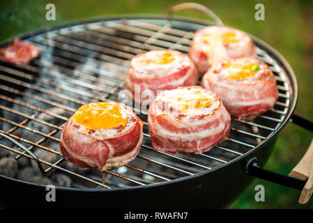 Making home made Beer Can Bacon Burgers on barbecue grill. Preparing stuffed patties, wrapped  in bacon and grilling on indirect heat in nature at bac Stock Photo