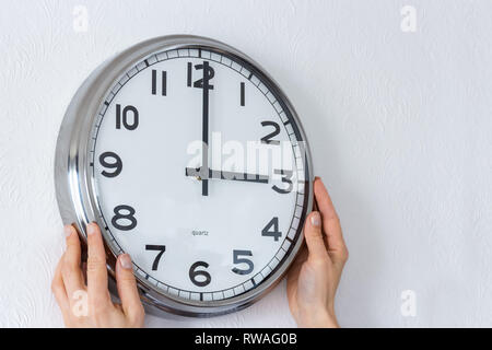 Woman hangs a big silver clock on the white wall. Stock Photo