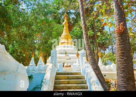 The white-golden carved stupa of Shwethalyaung Buddha Temple is surrounded by lush garden greenery, Bago, Myanmar. Stock Photo