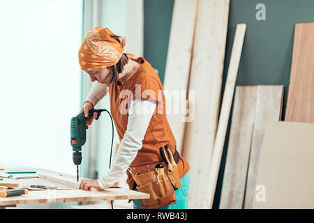 Female carpenter using electric drill in woodwork carpentry workshop, selective focus Stock Photo