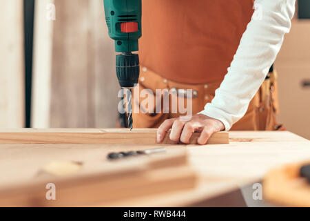 Female carpenter using electric drill in woodwork carpentry workshop, selective focus Stock Photo