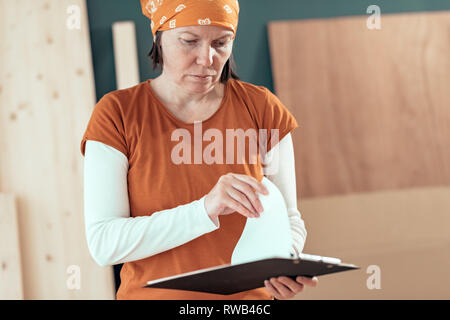 Female carpenter reading DIY project notes in small business woodwork workshop Stock Photo