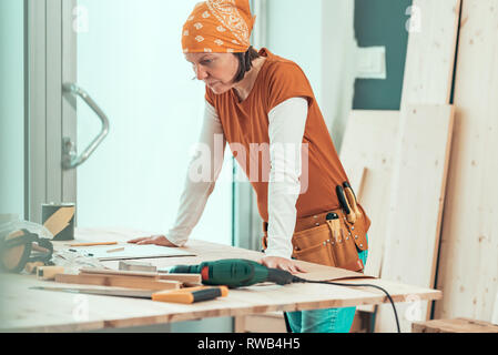 Female carpenter with bandanna posing in woodwork workshop, small business entrepreneur at work place Stock Photo