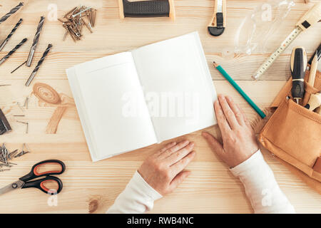 Female carpenter reading DIY project instruction manual in small business woodwork workshop, top view Stock Photo